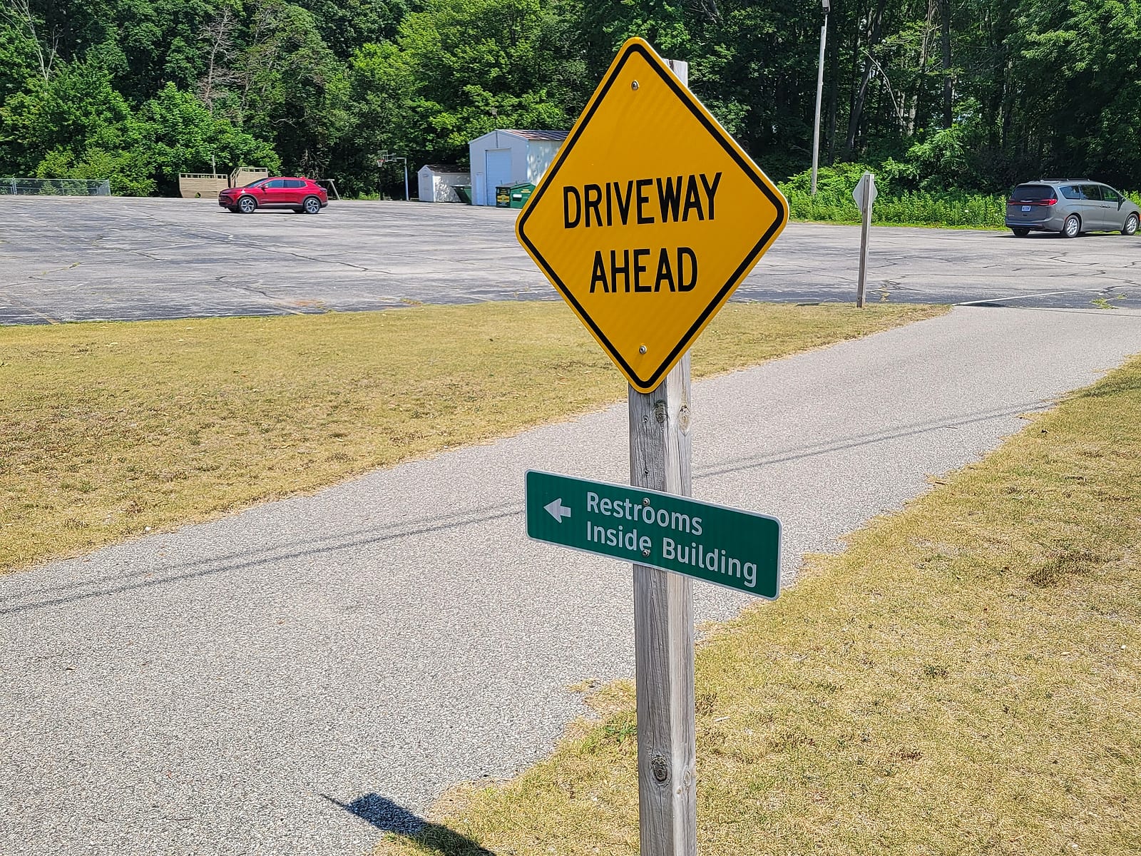 Green Restrooms Inside Building sign and yellow driveway warning on a post beside the Berry Junction Trail at First Lutheran Church in Muskegon