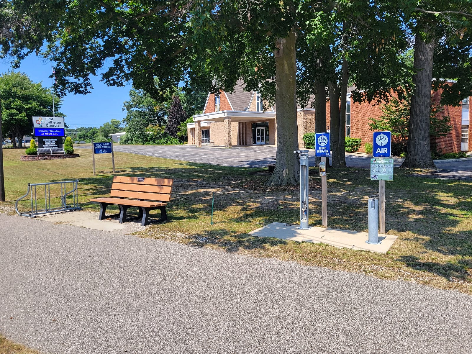 First Lutheran Church on Whitehall Road in Muskegon with its trailside bench, bike rack, All Are Welcome sign, bike repair stand, and air pump beside the Berry Junction Trail