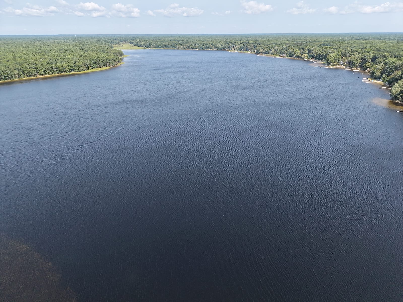 Aerial view down the full length of Duck Lake facing east, with forested state park shoreline on the north side and cottages along the south shore