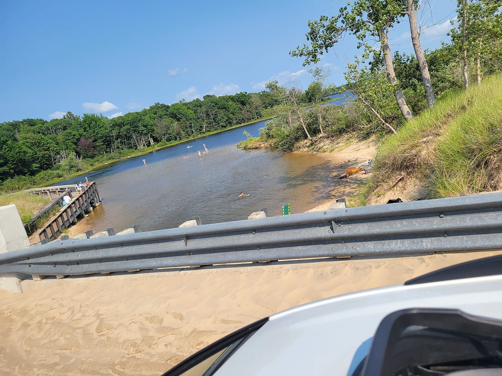Families floating and wading in the warm lagoon at the Duck Lake outlet, seen from the Scenic Drive bridge