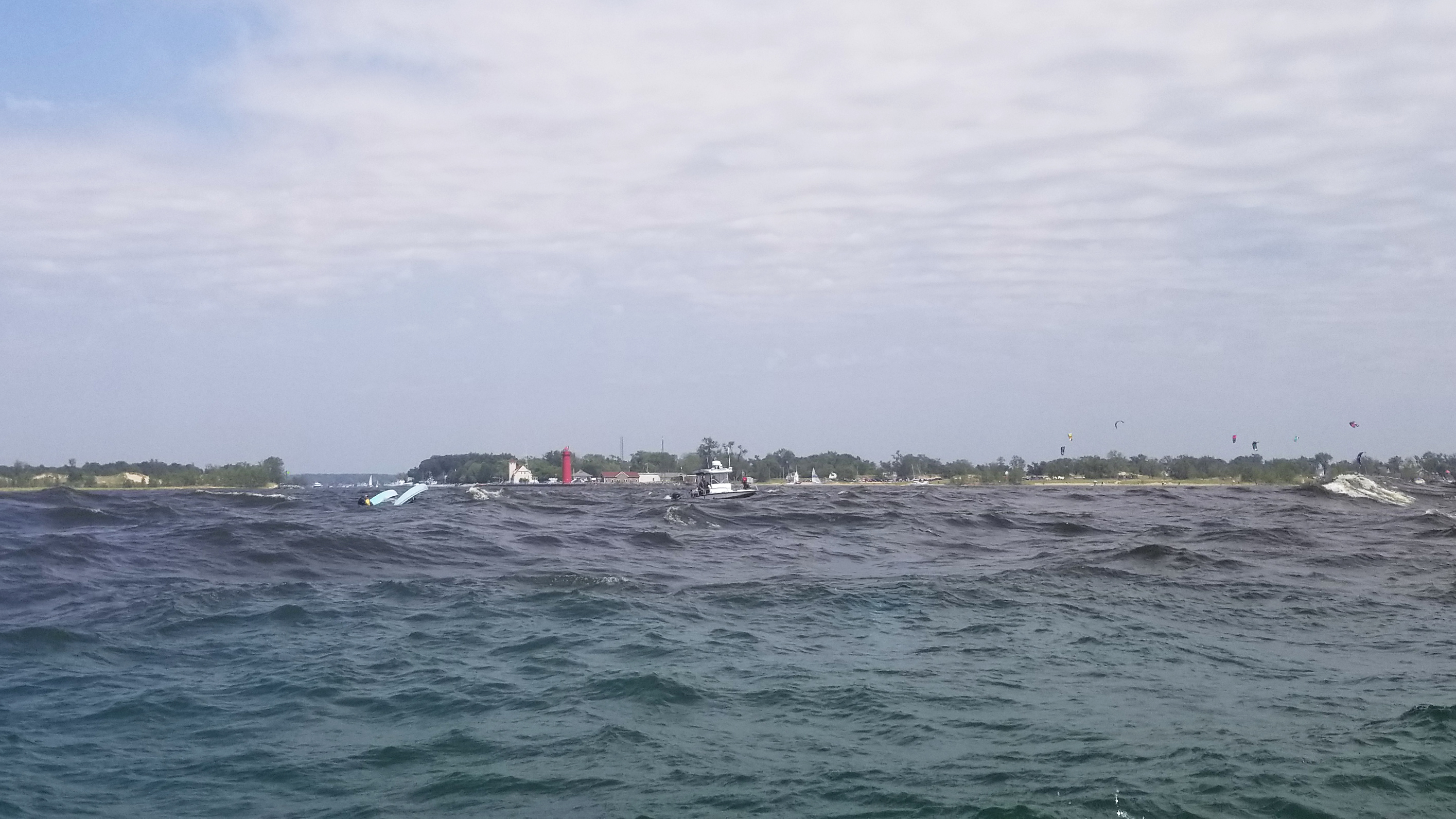 Capsized boat and water rescue in the Muskegon channel waves while kitboarders ride nearby - showing the power of Lake Michigan