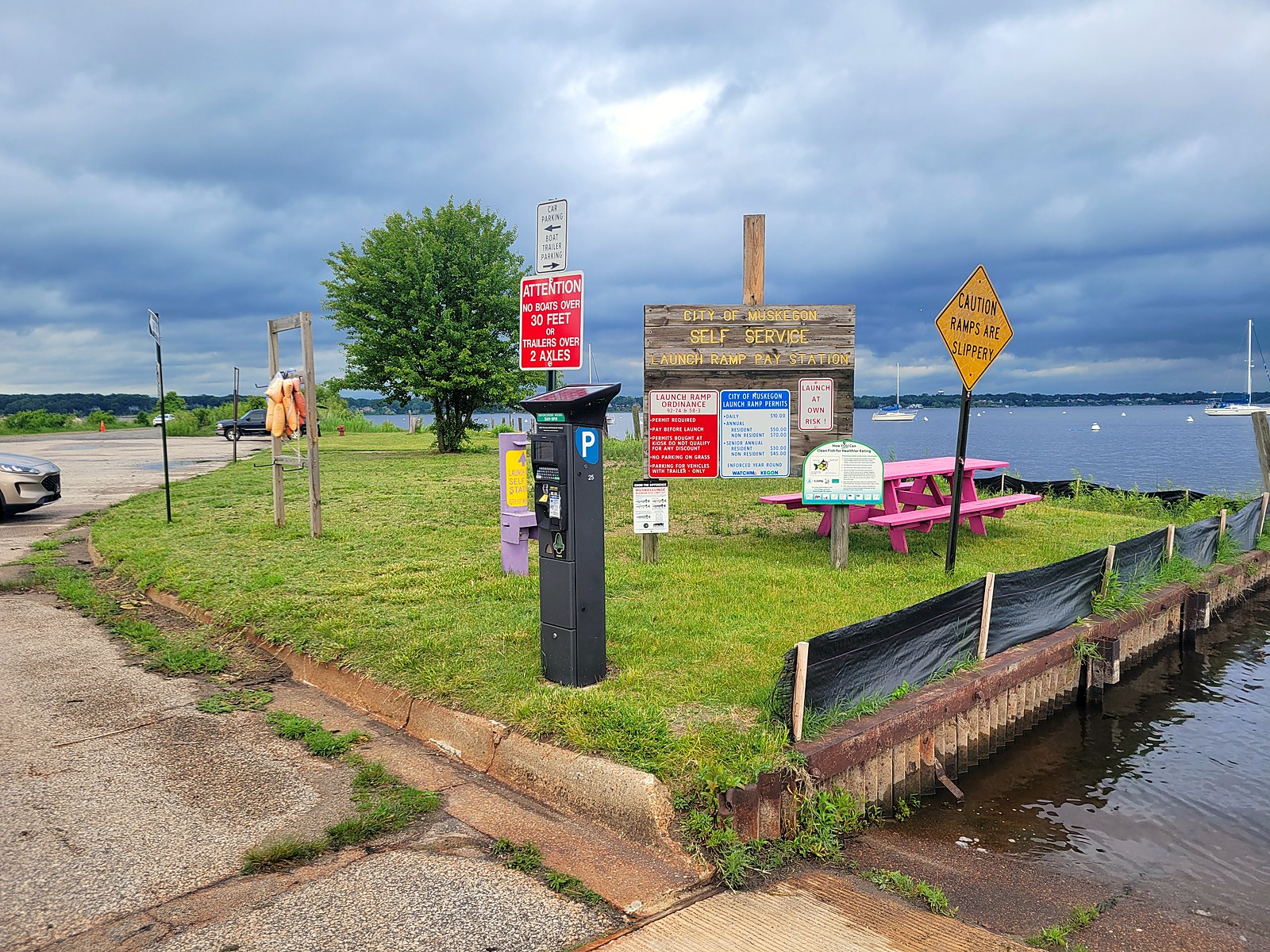 City of Muskegon self-service launch ramp pay station at the Hartshorn ramp, with posted boards showing the daily and annual launch permit fees, a 30-foot boat and 2-axle trailer limit, and a ramps-are-slippery caution sign.
