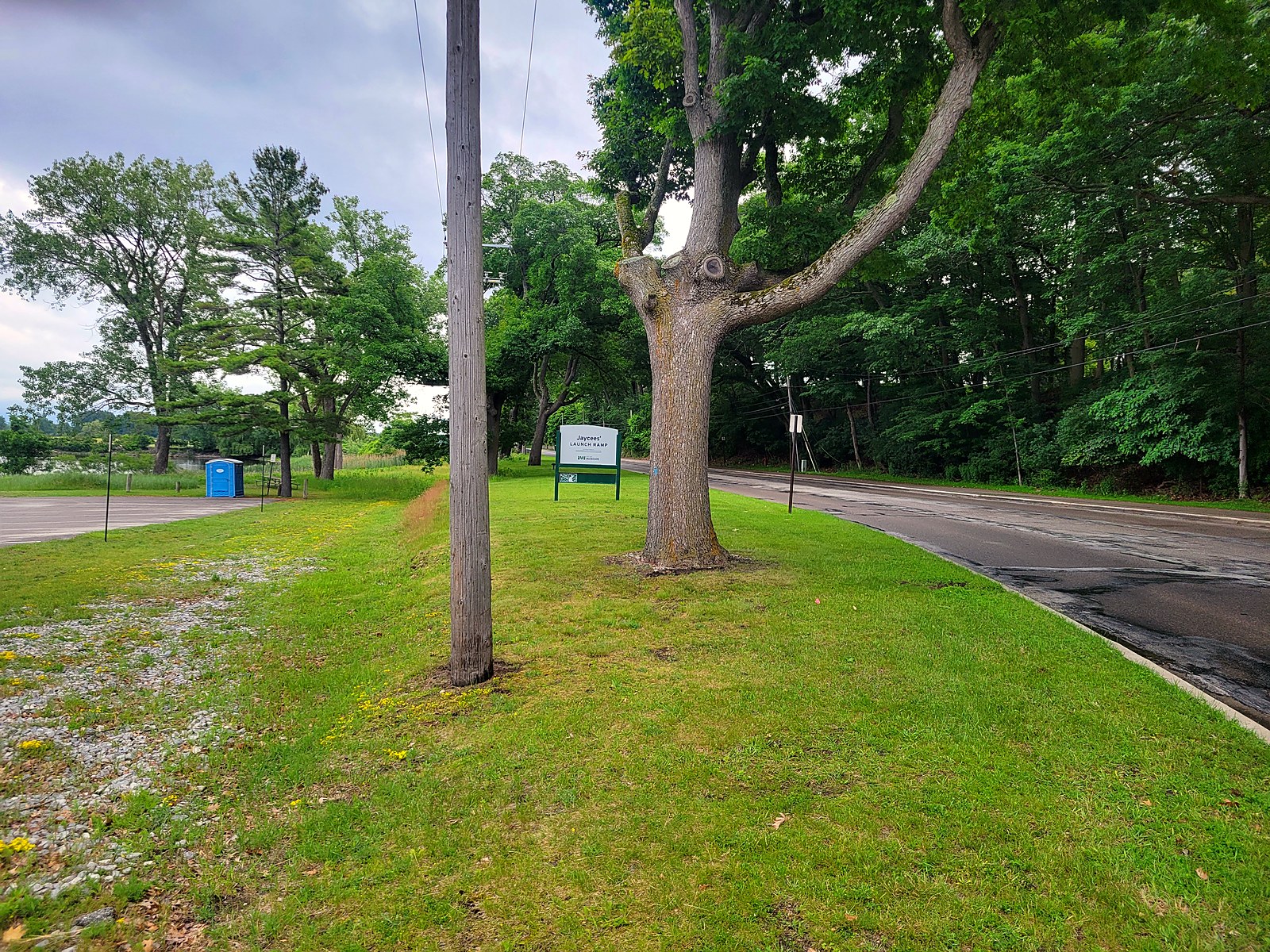 The Jaycees' Launch Ramp entrance sign, a City of Muskegon park sign on a grassy strip along Lakeshore Drive, with a large tree and the parking lot beyond.