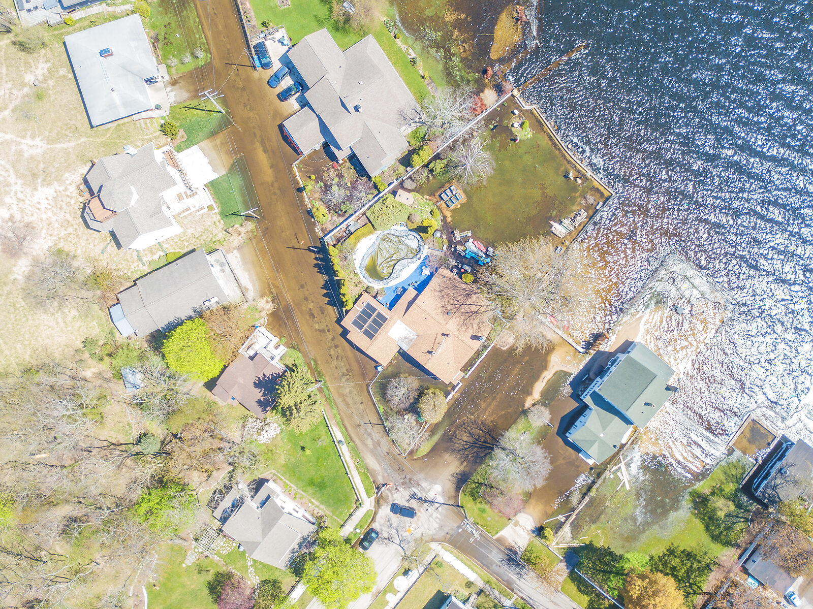 Aerial drone view of 2020 high-water flooding along the Muskegon Lake shoreline, with floodwater over the road, lakefront yards, and seawalls, even surrounding a backyard pool, as the lake rose.