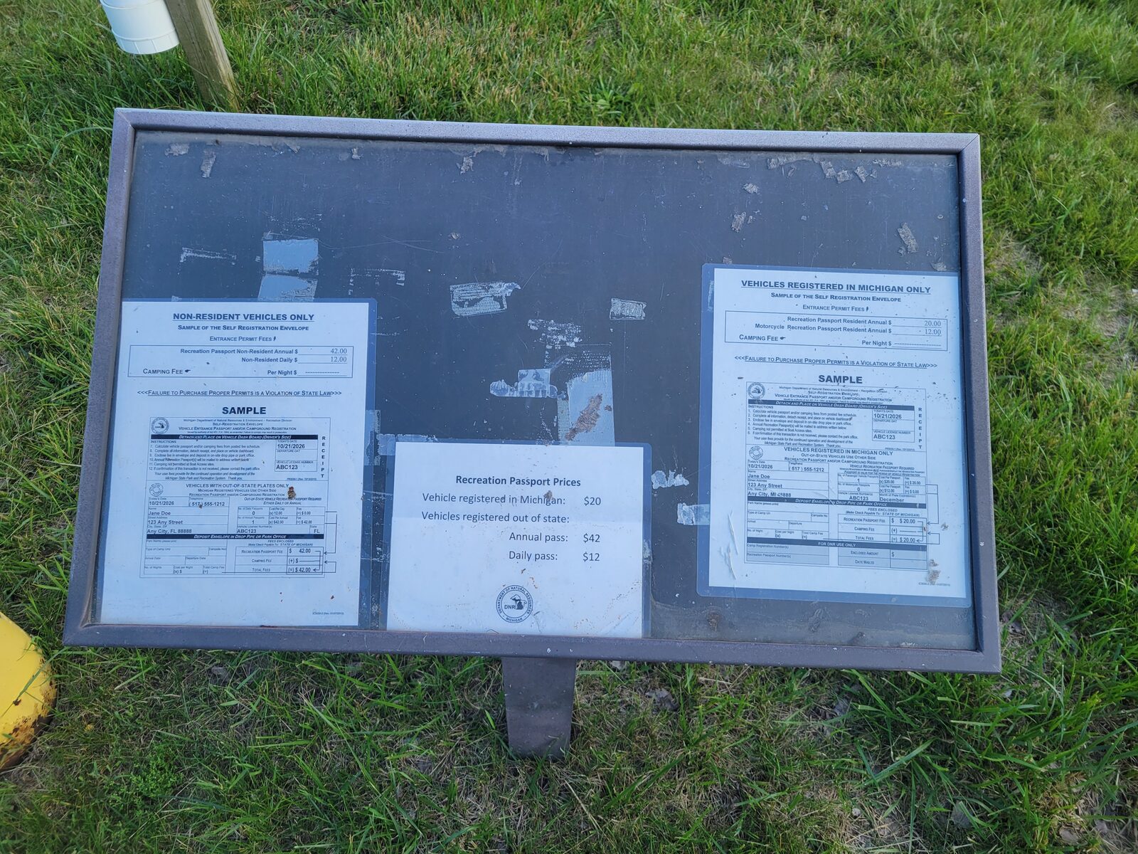 The self-registration fee board at the Snug Harbor launch listing Michigan Recreation Passport prices: twenty dollars for Michigan-registered vehicles, and forty-two dollars annual or twelve dollars daily for out-of-state vehicles.