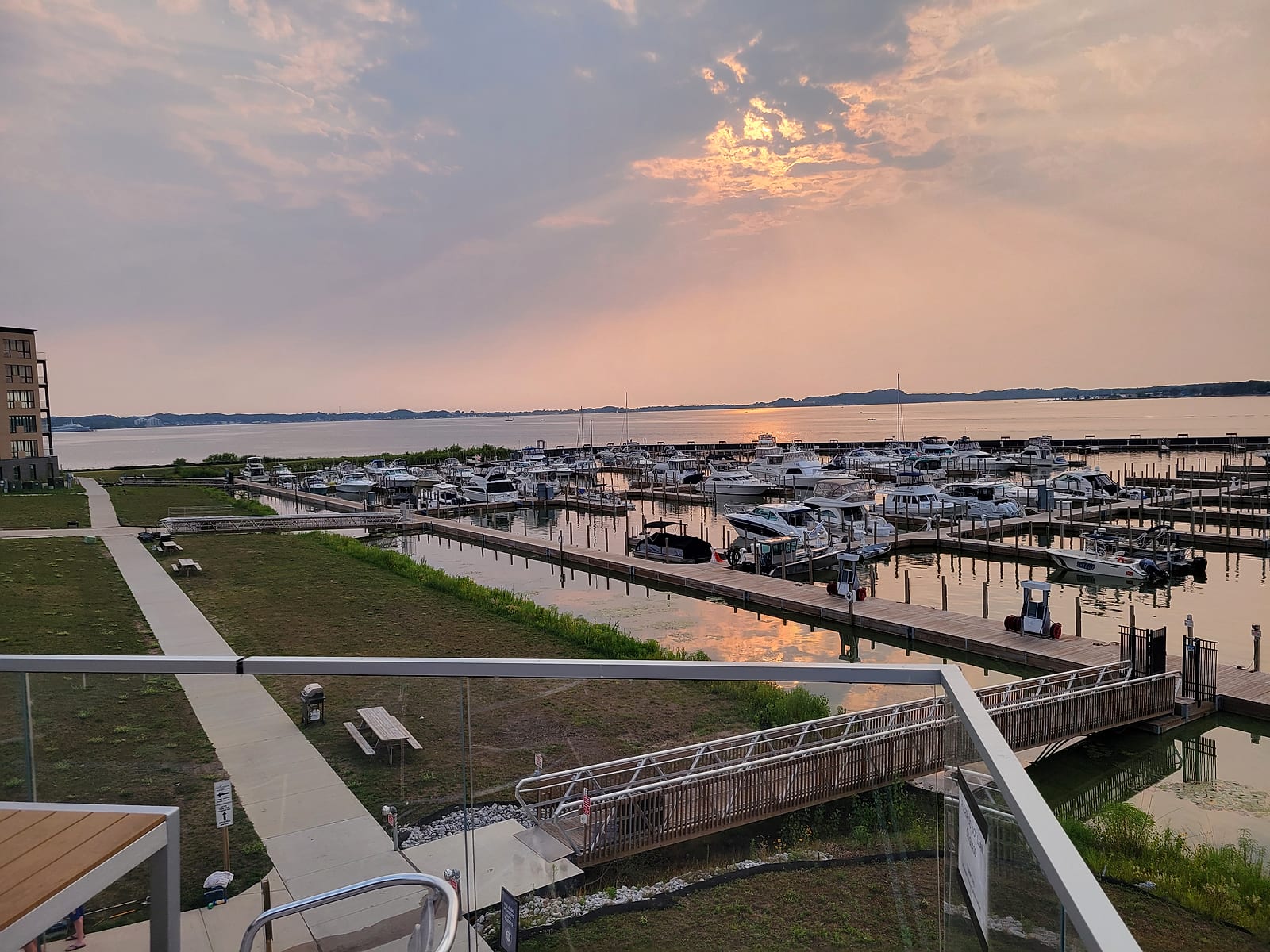 Adelaide Pointe Marina's floating docks and boat slips on Muskegon Lake at sunset in August 2026, seen from the second-floor Muskegon Brewing Company restaurant deck