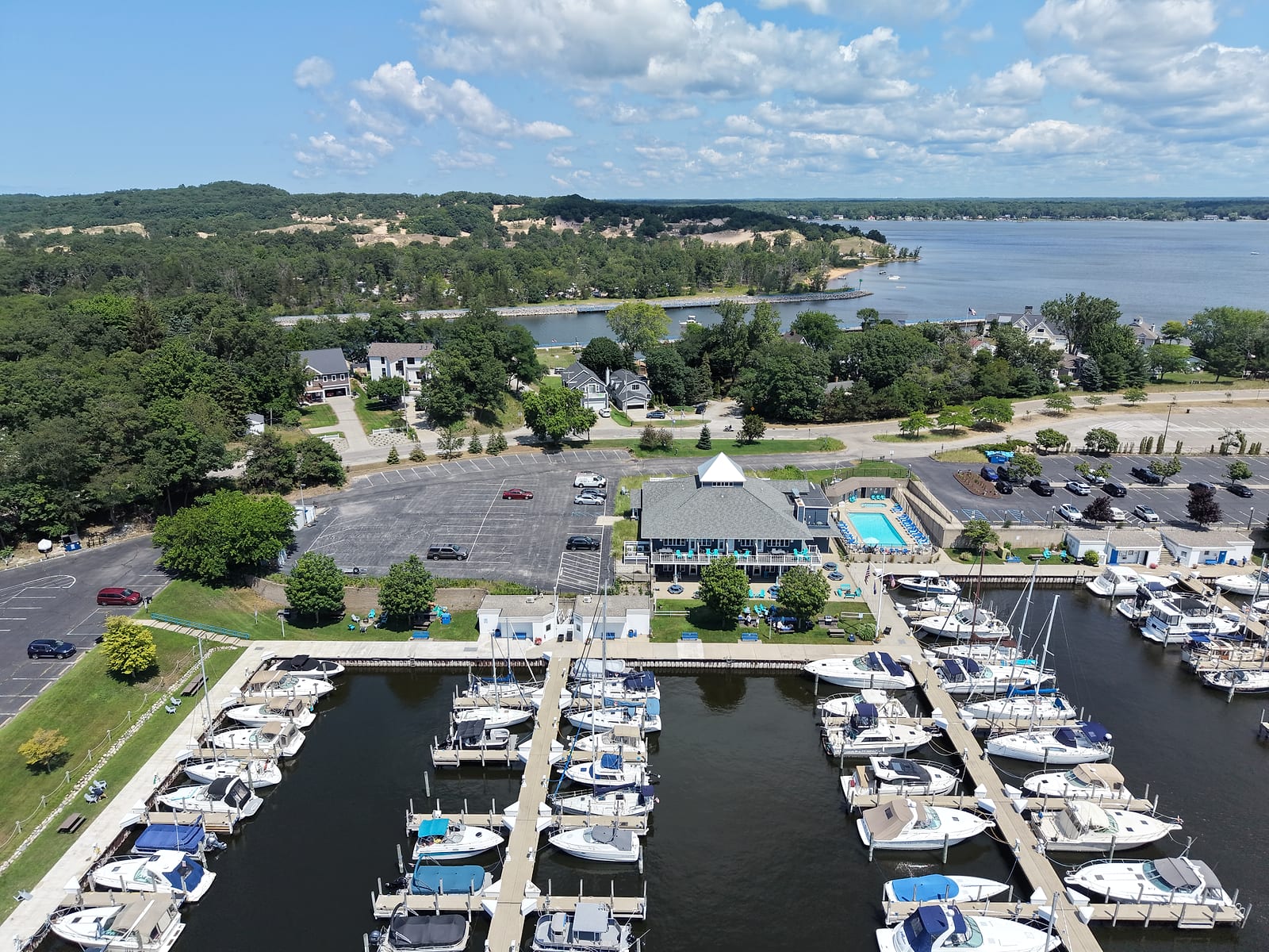 July 2026 aerial drone view of The Pidge Inn at Harbour Towne in Muskegon: the pyramid-roofed boutique hotel and its pool beside Harbour Towne Marina's slips, with the marina's entrance channel and Muskegon Lake beyond.