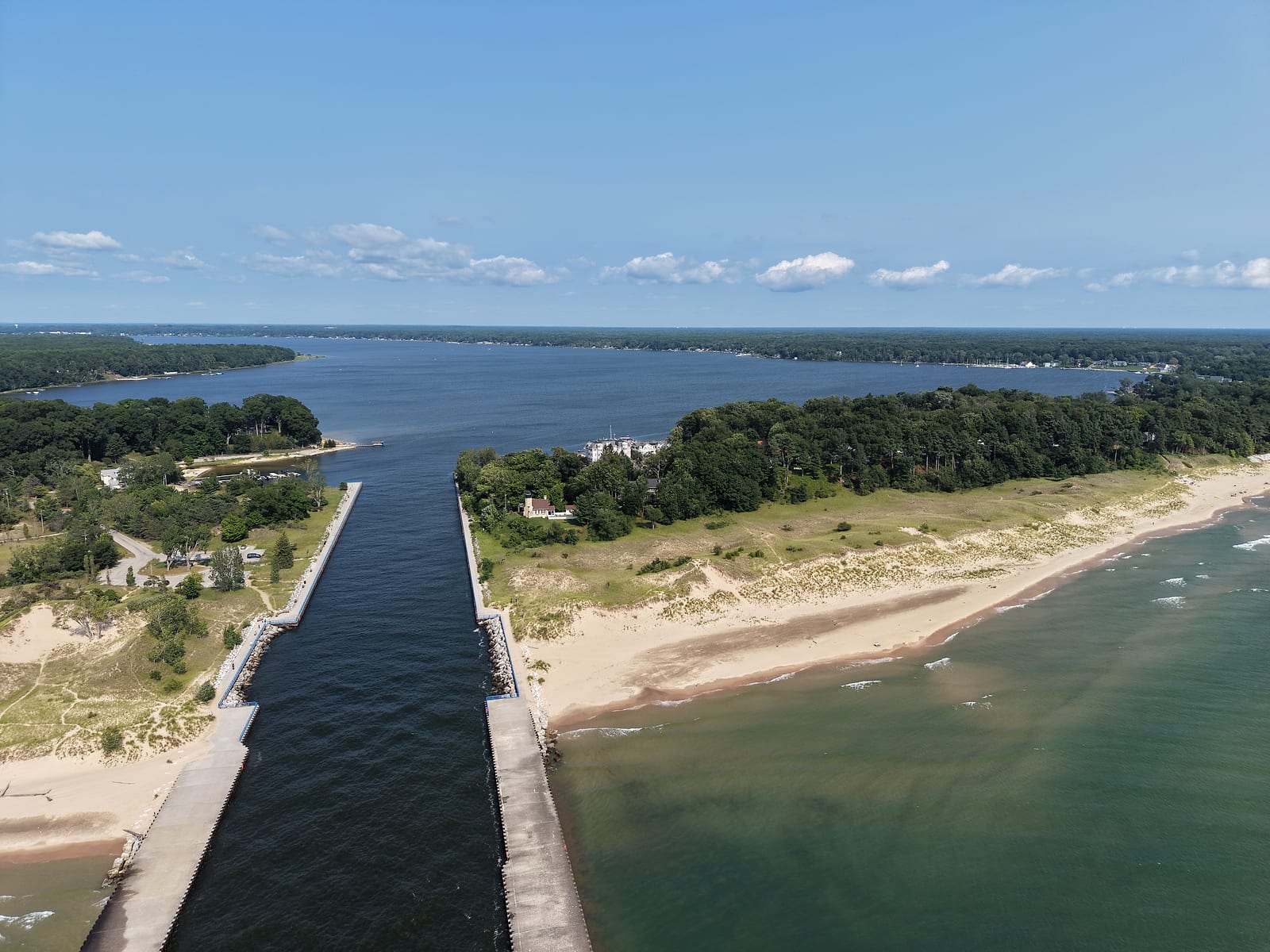 Aerial view over the White Lake channel at the Lake Michigan shore, with the White River Light Station on the south point and White Lake stretching inland toward Whitehall and Montague