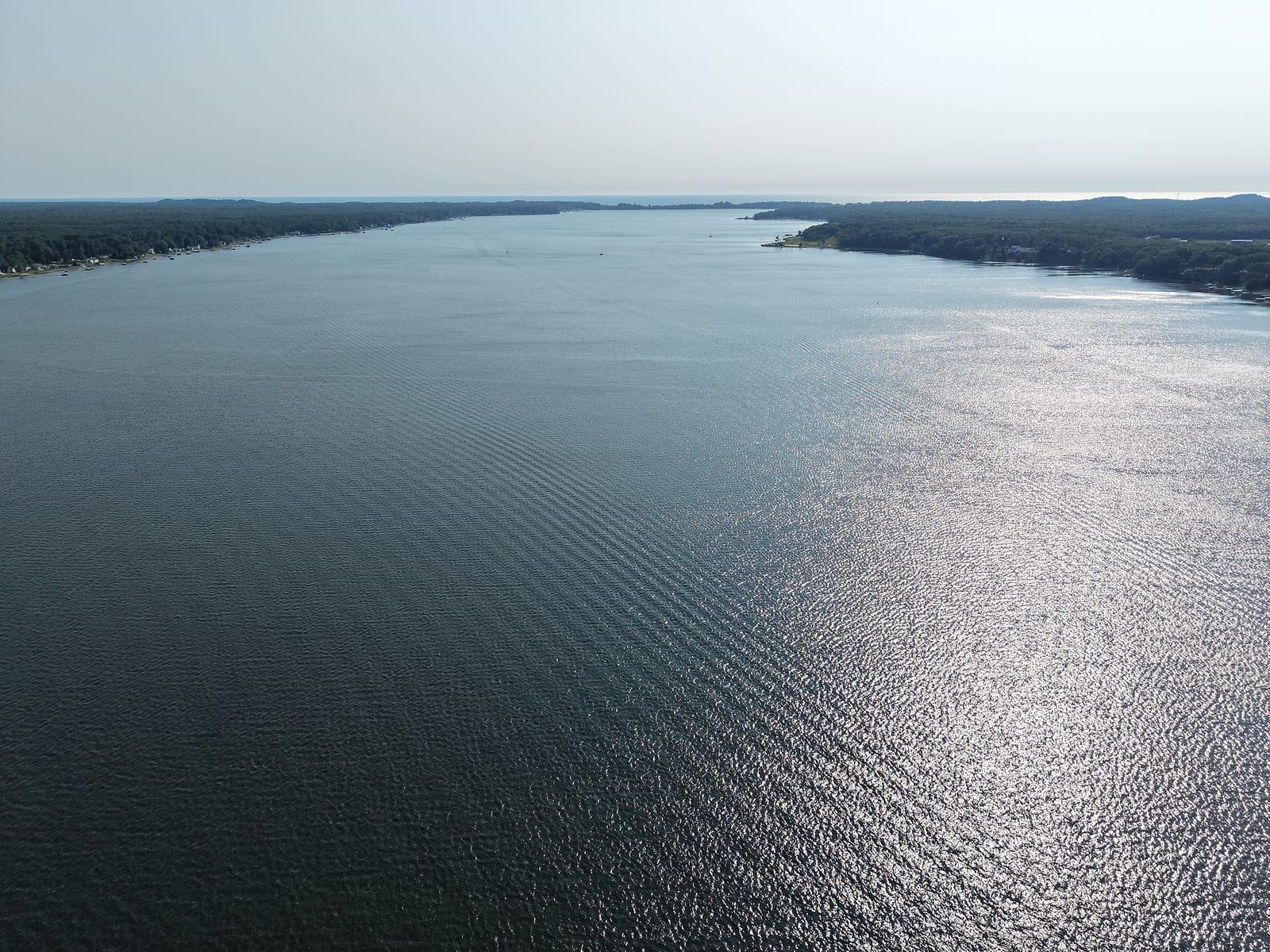 Aerial view down the length of White Lake between its wooded shorelines toward Lake Michigan on the horizon