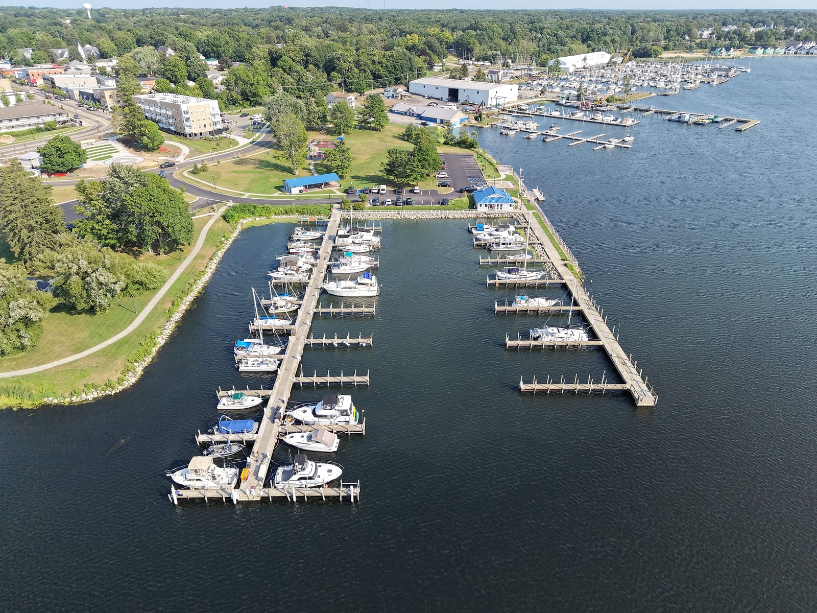 Aerial view of the White Lake Municipal Marina in Whitehall with its slips, blue-roofed marina office, Goodrich Park, and downtown beyond