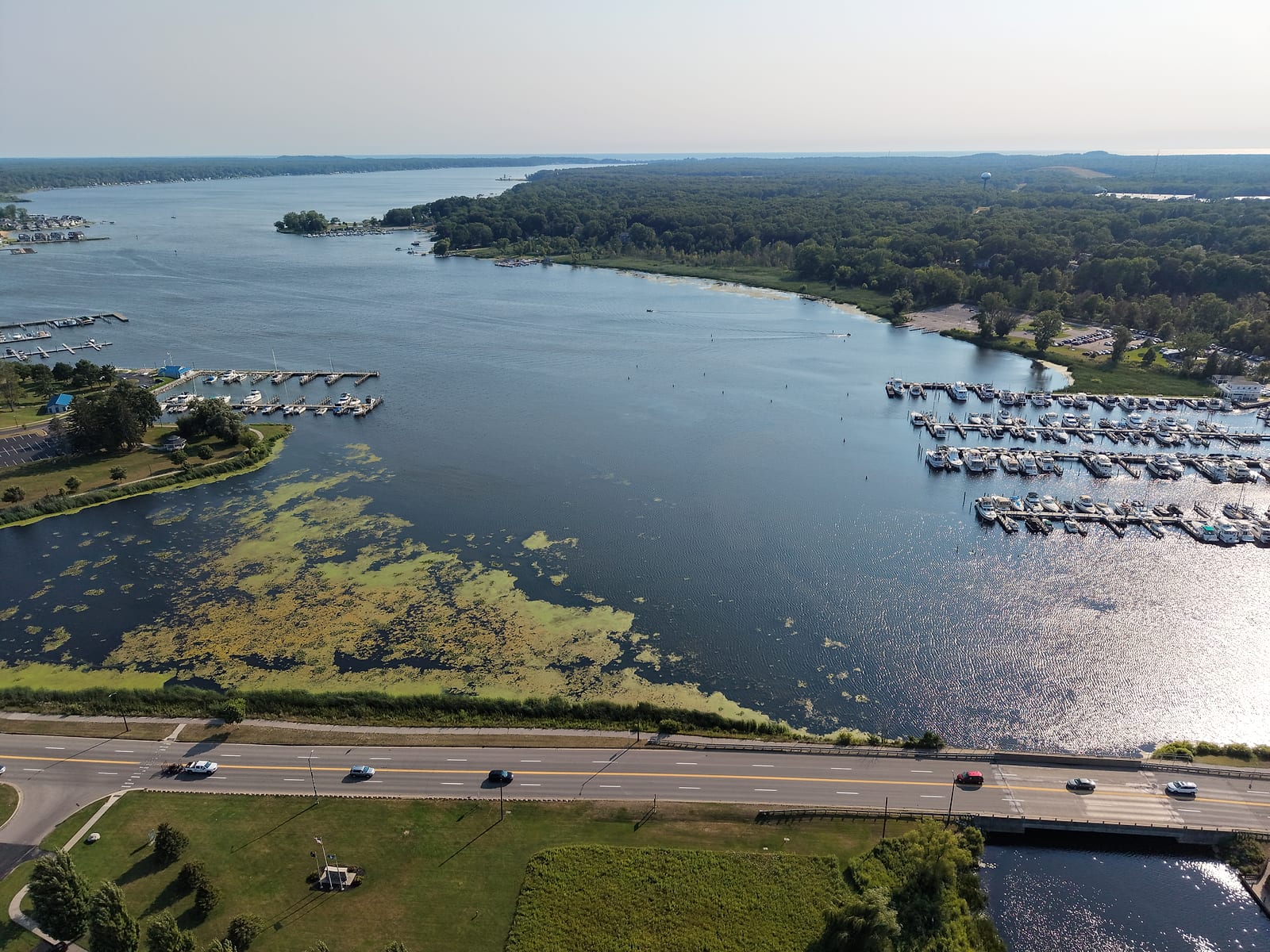 Aerial view of upper White Lake from above the causeway with green weed mats along the shallow river end and marinas on both shores